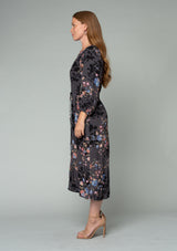 [Color: Grey/Dusty Blue] A side facing image of a red headed model wearing a lightweight bohemian mid length dress in a grey and blue floral print. With three quarter length sleeves, a button front, side pockets, and an adjustable drawstring waist. 