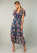 [Color: Navy/Rust] A full body front facing image of a blonde model wearing a sheer chiffon bohemian maxi dress in a navy blue and rust red floral print. Wit short flutter sleeves, a long tiered skirt, and an adjustable drawstring waist.