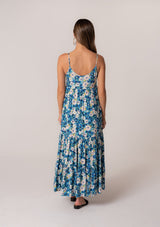 [Color: Dusty Teal/Blue] A back facing image of a brunette model wearing a flowy summer maxi dress in a blue floral print. With adjustable spaghetti straps, a scalloped edge v neckline, a button front top, a flowy tiered skirt, and side pockets. 