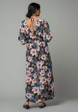 [Color: Charcoal/Rose] A back facing image of a brunette model wearing a charcoal grey and pink floral print bohemian resort maxi dress with half length kimono sleeves, an open back with tie closure, and a smocked elastic waist. 