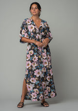 [Color: Charcoal/Rose] A front facing image of a brunette model wearing a charcoal grey and pink floral print bohemian resort maxi dress with half length kimono sleeves, an open back with tie closure, and a smocked elastic waist. 