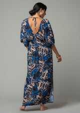 [Color: Cobalt/Tan] A back facing image of a brunette model wearing a navy blue and tan butterfly wing printed resort maxi dress with half length kimono sleeves, a smocked elastic waist, an open back with tie closure, and a sexy surplice v neckline. 