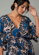 [Color: Cobalt/Tan] A close up front facing image of a brunette model wearing a navy blue and tan butterfly wing printed resort maxi dress with half length kimono sleeves, a smocked elastic waist, an open back with tie closure, and a sexy surplice v neckline. 