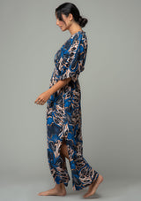 [Color: Cobalt/Tan] A side facing image of a brunette model wearing a navy blue and tan butterfly wing printed resort maxi dress with half length kimono sleeves, a smocked elastic waist, an open back with tie closure, and a sexy surplice v neckline. 