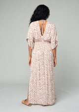 [Color: Ivory/Sand] A back facing image of a brunette model wearing a best selling resort maxi dress in an ivory and brown bohemian diamond print. With short kimono sleeves, a smocked elastic waist, a v neckline, side slits, and an open back with tie closure. 