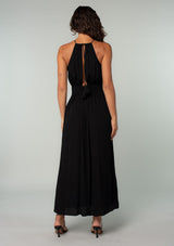 [Color: Black] A back facing image of a brunette model wearing a bohemian black halter maxi dress. A holiday maxi dress with thin spaghetti straps, a back keyhole, a halter neckline with adjustable back tassel ties, light catching beaded accents, a half smocked elastic waist at the back, and a long flowy skirt. 