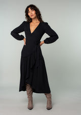 [Color: Black] A full body front facing image of a brunette model wearing a black maxi wrap dress with long sleeves, a ruffle trimmed tiered high low hemline, and a side tie closure. 