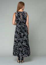 [Color: Black/Lavender] A back facing image of a red headed model wearing a black and lavender purple floral print chiffon maxi dress. A sleeveless holiday maxi dress with a long tiered skirt and an open back keyhole with tie closure.