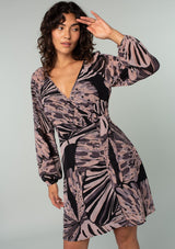 [Color: Black/Natural] A front facing image of a brunette model wearing a bohemian chiffon mini wrap dress in a black and natural abstract butterfly wing print. With long sleeves, a plunging deep v neckline, and a wrap front with side tie closure and o ring detail. 