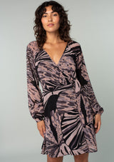 [Color: Black/Natural] A front facing image of a brunette model wearing a bohemian chiffon mini wrap dress in a black and natural abstract butterfly wing print. With long sleeves, a plunging deep v neckline, and a wrap front with side tie closure and o ring detail. 