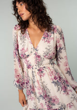 [Color: Natural/Wine] A close up front facing image of a brunette model wearing a sheer chiffon bohemian mini dress in a natural and wine pink floral print. With long sleeves, a button front top, ruffle details, and a tiered skirt. 