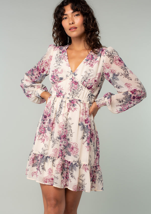 [Color: Natural/Wine] A front facing image of a brunette model wearing a sheer chiffon bohemian mini dress in a natural and wine pink floral print. With long sleeves, a button front top, ruffle details, and a tiered skirt. 
