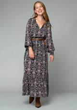 [Color: Black/Rose] A full body front facing image of a red headed model wearing a classic bohemian maxi dress in a black and pink paisley print. With long sleeves, side slits, and an elastic waist. 