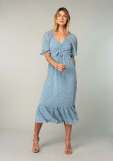 [Color: Dusty Blue/Natural] A full body front facing image of a blonde model wearing a bohemian blue mid length dress in lightweight sheer chiffon. With short flutter sleeves, a flattering top with gathered details, and a flowy tiered skirt. 