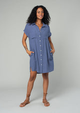 [Color: Dark Denim] A front facing image of a brunette model wearing a loose and relaxed fit blue mini shirt dress. With short cuffed sleeves, a button front, front patch pockets, and side pockets. 