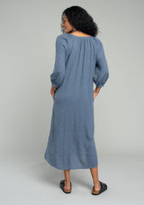 [Color: Navy] A back facing image of a brunette model wearing a loose, relaxed fit bohemian resort midi dress in navy blue. With three quarter length sleeves, a split v neckline, side pockets, and a loose fit. 