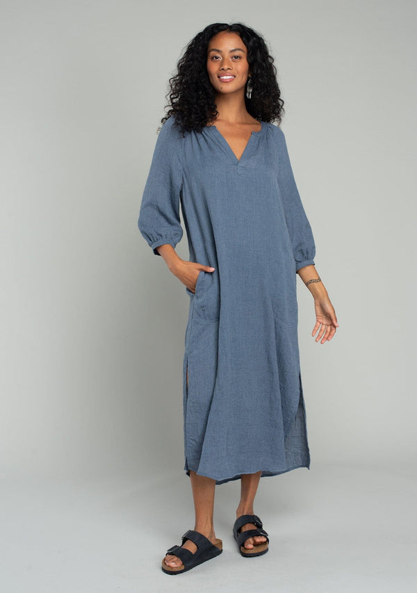 [Color: Navy] A front facing image of a brunette model wearing a loose, relaxed fit bohemian resort midi dress in navy blue. With three quarter length sleeves, a split v neckline, side pockets, and a loose fit. 
