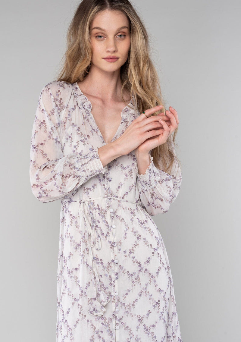[Color: Ivory/Plum] A close up front facing image of a blonde model wearing a romantic bohemian mid length chiffon dress in an ivory and plum purple floral print. A spring dress with long sleeves, a self covered button front, a v neckline, a flowy tiered skirt, and a self tie waist belt. 