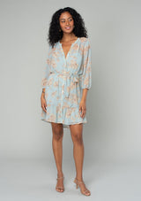 [Color: Dusty Blue/Natural] A front facing image of a brunette model wearing a sheer chiffon bohemian mini dress in a dusty blue and natural floral print. With sheer three quarter length sleeves, a button front, a tiered skirt, and a self tie waist belt. 