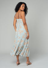 [Color: Dusty Blue/Natural] A back facing image of a brunette model wearing a pretty chiffon mid length slip dress in a dusty blue and natural floral print. With adjustable spaghetti straps, a flowy tiered skirt, a half smocked elastic waist at the back, an empire waist, and a gathered top with drawstring. 