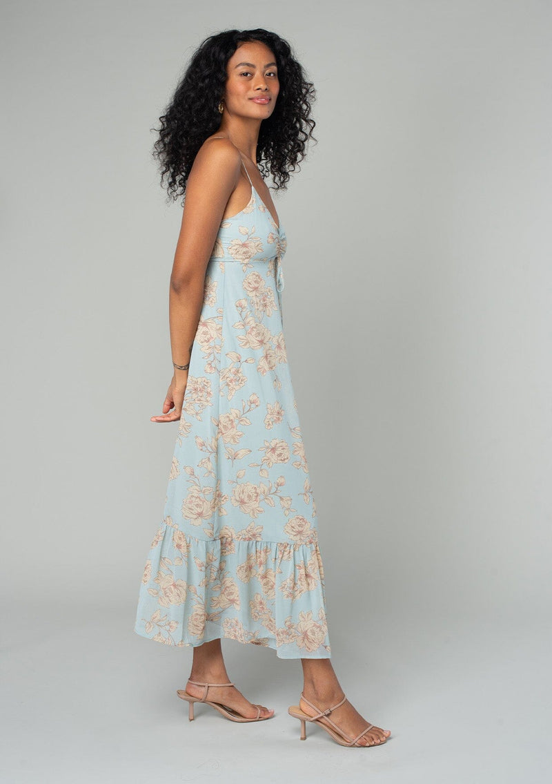 [Color: Dusty Blue/Natural] A side facing image of a brunette model wearing a pretty chiffon mid length slip dress in a dusty blue and natural floral print. With adjustable spaghetti straps, a flowy tiered skirt, a half smocked elastic waist at the back, an empire waist, and a gathered top with drawstring. 