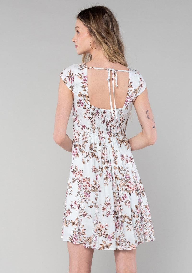 [Color: Mint/Rose] A back facing image of a blonde model wearing a spring bohemian mini dress in a mixed pink floral print. With short cap sleeves, a square neckline, an empire waist, a paneled skirt, and a back tie closure. 