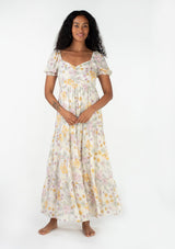 [Color: Natural/Pink] A front facing image of a brunette model wearing a bohemian spring maxi dress in an ivory, pink, and yellow vintage inspired floral print. With a sweetheart neckline, short puff sleeves, an empire waist, a flowy tiered skirt, and a smocked elastic bodice at the back. Designed in a pretty textured swiss dot. 