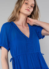 [Color: Cobalt] A close up front facing image of a blonde model wearing a romantic and flowy bright blue sheer chiffon bohemian maxi dress. With short sleeves, a v neckline, a high low hemline, and a drawstring waist with adjustable side ties.