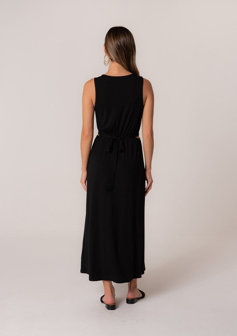 [Color: Black] A back facing image of a brunette model wearing a soft and stretchy knit sleeveless maxi dress in black. With a v neckline, sexy side waist cutouts, and a self tie belt. 
