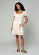 [Color: Vanilla] A full body front facing image of a brunette model wearing a cream colored bohemian mini dress in a textured stripe. With sheer short puff sleeves, a slim fitting smocked bodice, a flowy tiered skirt, and a square neckline. 