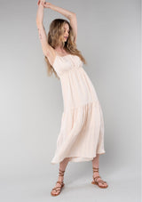 [Color: Natural] A full body front facing image of a blonde model wearing a bohemian spring maxi tank dress in a natural shadow stripe. With adjustable spaghetti straps, a round neckline, a tiered flowy skirt, a back cutout detail, and a back tie waist detail. 