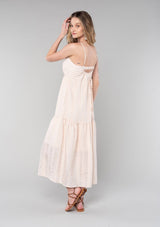[Color: Natural] A back facing image of a blonde model wearing a bohemian spring maxi tank dress in a natural shadow stripe. With adjustable spaghetti straps, a round neckline, a tiered flowy skirt, a back cutout detail, and a back tie waist detail. 