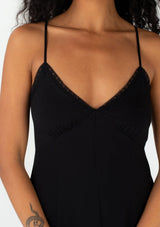 [Color: Black] A close up front facing image of a brunette model wearing a sexy spring slip dress in black. With adjustable spaghetti straps, a v neckline, lace trim, a half elastic waist at the back, and a flowy paneled mid length skirt. 