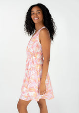 [Color: Peach/Light Pink] A side facing image of a brunette model wearing a pretty sleeveless spring mini dress in a pink floral print. With a surplice v neckline, an elastic waist, and a double layered tiered skirt. 