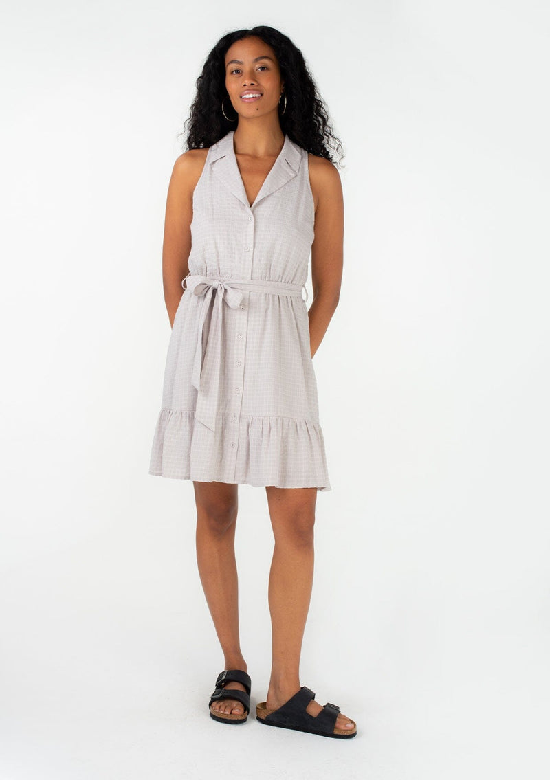 [Color: Dove] A front facing image of a brunette model wearing a retro inspired grey checkered cotton seersucker sleeveless mini dress. With a collared neckline, a flowy tiered skirt, an elastic waist, a tie waist belt, and a self covered button front. 