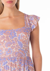 [Color: Ivory/Coral] A close up front facing image of a blonde model wearing a bohemian spring mini dress in a retro inspired purple floral print. With short ruffled cap sleeves, a square neckline, a ruffle trimmed tiered skirt, an open back with tie closure, and a smocked bodice at the back. 