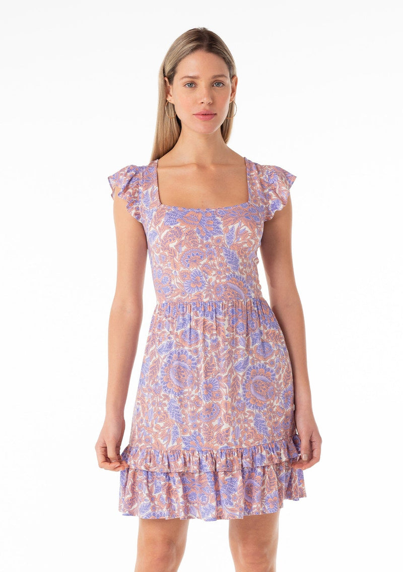 [Color: Ivory/Coral] A front facing image of a blonde model wearing a bohemian spring mini dress in a retro inspired purple floral print. With short ruffled cap sleeves, a square neckline, a ruffle trimmed tiered skirt, an open back with tie closure, and a smocked bodice at the back. 