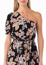 [Color: Black/Pink] A close up front facing image of a blonde model wearing a bohemian spring maxi dress in a tropical pink floral print. With a one shoulder top, a puff sleeve, a flowy tiered skirt, a side slit, an elastic waist, and a tie waist belt. 