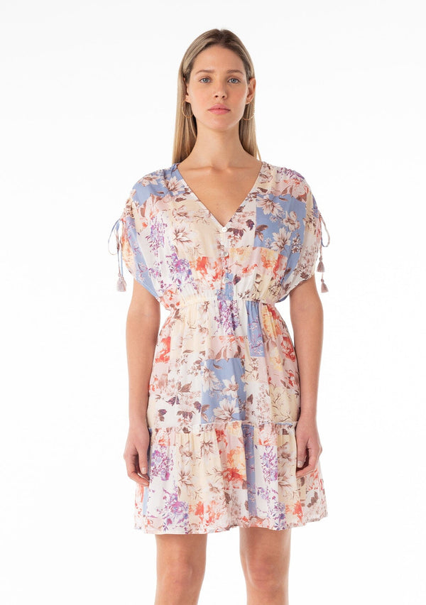 [Color: Natural/Rust] A front facing image of a blonde model wearing a bohemian spring cotton mini dress in a pink and blue floral print. With short gathered sleeves, tassel ties, a v neckline, a button front top, a ruffle trimmed tiered skirt, and a back keyhole with single button closure.