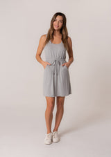 [Color: Heather Grey] A front facing image of a brunette model wearing a sporty sleeveless lounge mini dress in heather grey. Designed in a soft bamboo knit with a scoop neckline, side pockets, and an adjustable drawstring waist. 