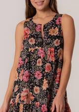[Color: Black/Fuchsia] A close up front facing image of a brunette model wearing a summer bohemian cotton mini dress in a black and pink floral print. A sleeveless mini dress with a roomy silhouette, a v neckline, and a tiered skirt. 