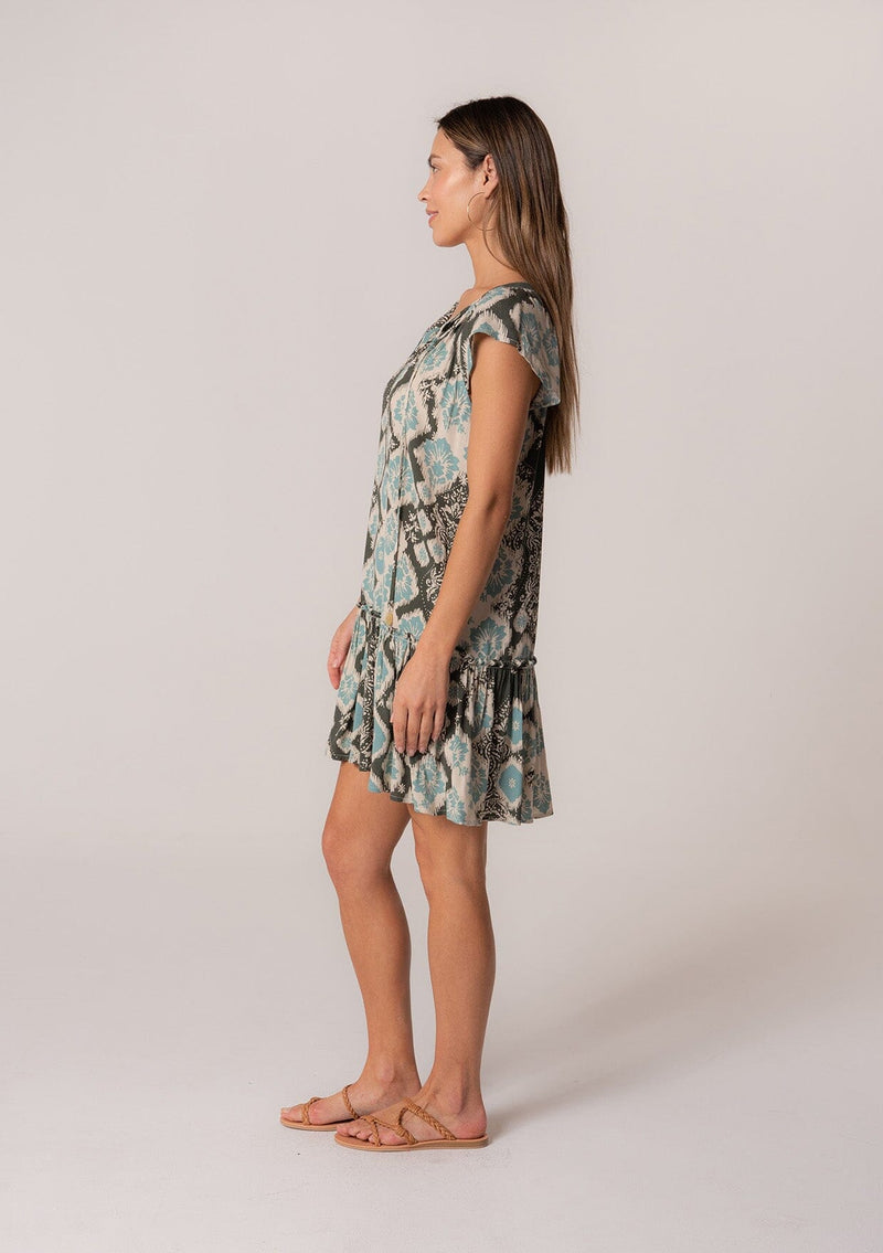 [Color: Black/Aqua] A side facing image of a brunette model wearing a lightweight summer mini dress in a green bohemian print. With short flutter sleeves, a split v-neckline with ties, and a ruffle trimmed tiered skirt. 
