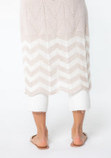 [Color: Linen/Ivory] A model wearing a beige and off white sweater knit tunic top with a long maxi length, side slits, and short sleeves. 
