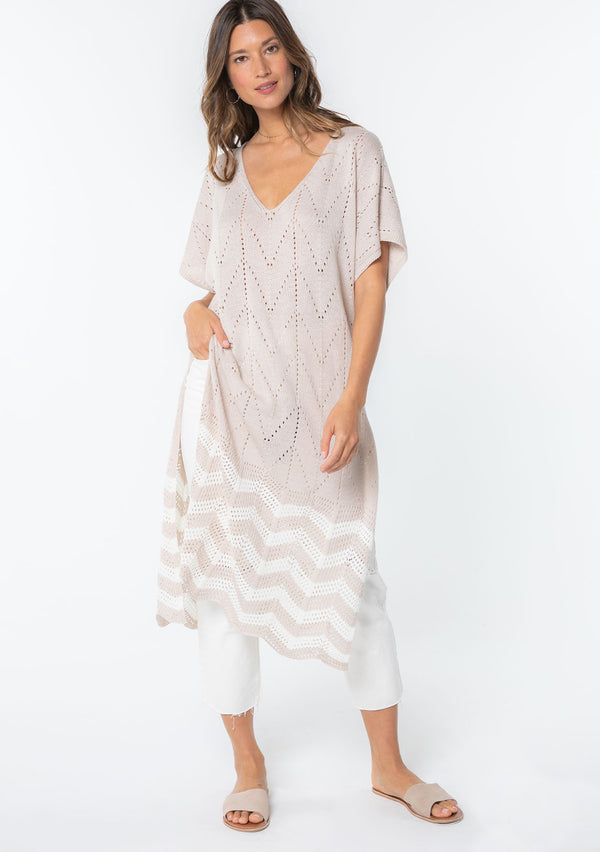 [Color: Linen/Ivory] A model wearing a beige and off white sweater knit tunic top with a long maxi length, side slits, and short sleeves. 