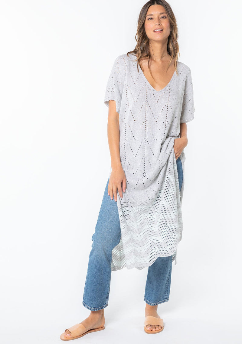 [Color: Lt Heather Grey/Ice] A model wearing a grey and light blue sweater knit tunic top with a long maxi length, side slits, and short sleeves. 