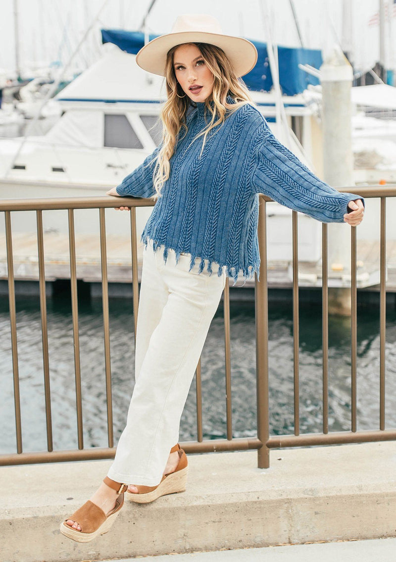 [Color: Indigo] A relaxed fit indigo cable knit sweater. A one hundred percent cotton pullover featuring a fringed hemline, a mock neckline, and a back vent detail.