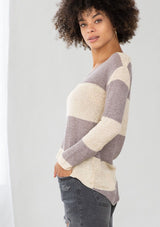 [Color: Dusty Orchid] A model wearing a dusty purple color block stripe sweater. With a wide v neckline, long sleeves, a dropped shoulder, and a high low hemline. 
