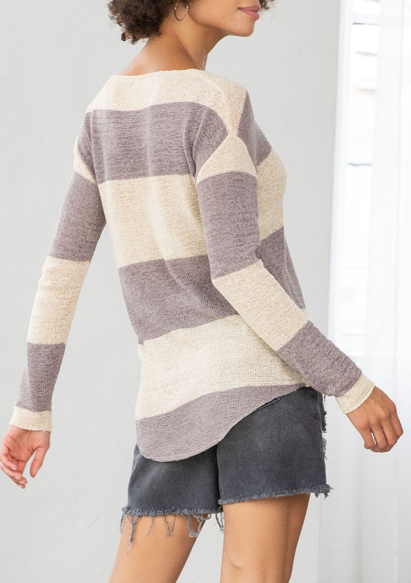 [Color: Dusty Orchid] A model wearing a dusty purple color block stripe sweater. With a wide v neckline, long sleeves, a dropped shoulder, and a high low hemline. 