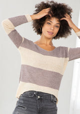 [Color: Dusty Orchid] A model wearing a dusty purple color block stripe sweater. With a wide v neckline, long sleeves, a dropped shoulder, and a high low hemline. 