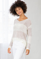 [Color: Silver/Ivory] A model wearing a silver and ivory color block stripe sweater. With a wide v neckline, long sleeves, a dropped shoulder, and a high low hemline. 